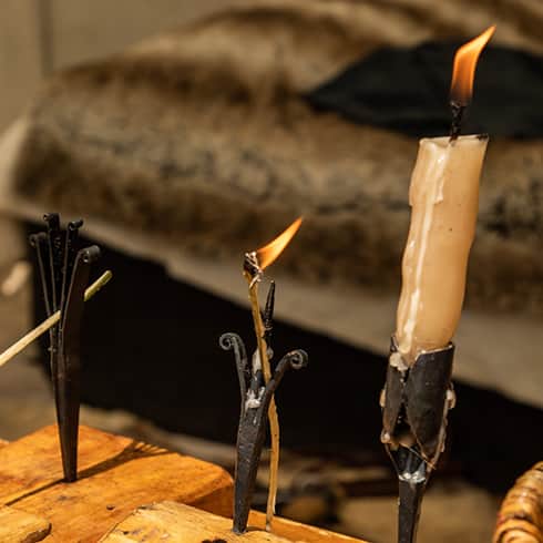 The image shows the heat and flame of a beeswax candle (right) and some rushlights erected in an iron pricket (left)