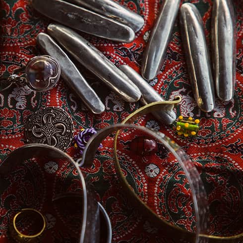 The image shows silver and bronze jewellery on a patterned silk background.