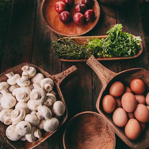 The image shows various food stuff ready for cooking. Eggs, Mushrooms, herbs and fruit.